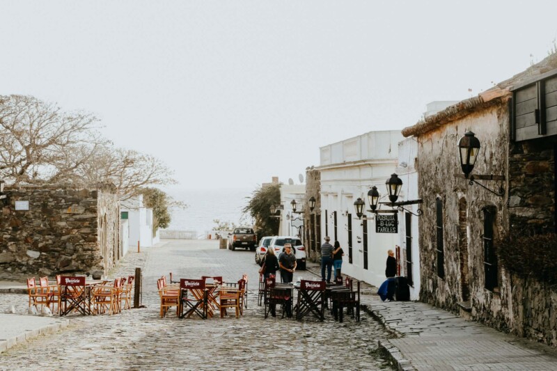 Tables and chairs on a cobblestone street by colonial buildings