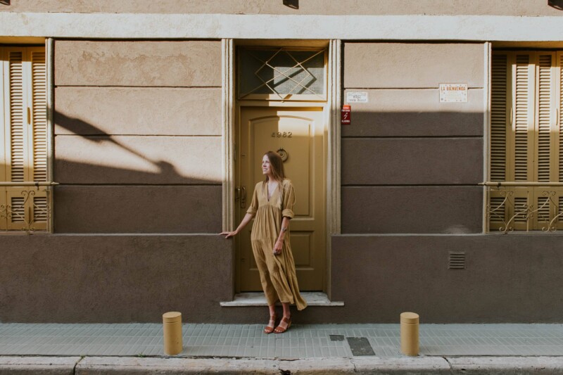A woman in a yellow dress stands in front of a monochrome beige home