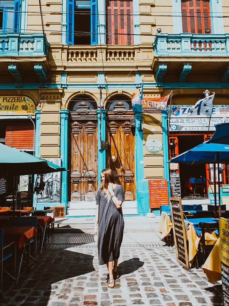 A woman walks down a cobblestone street in front of a yellow building