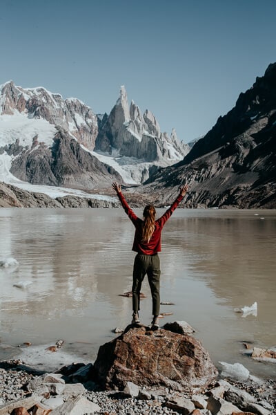 A woman stands with arms outstretched on a rock in front of a lagoon