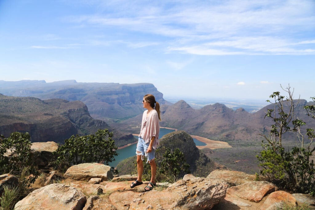 A woman stands on the edge of a cliff over a green ganyon