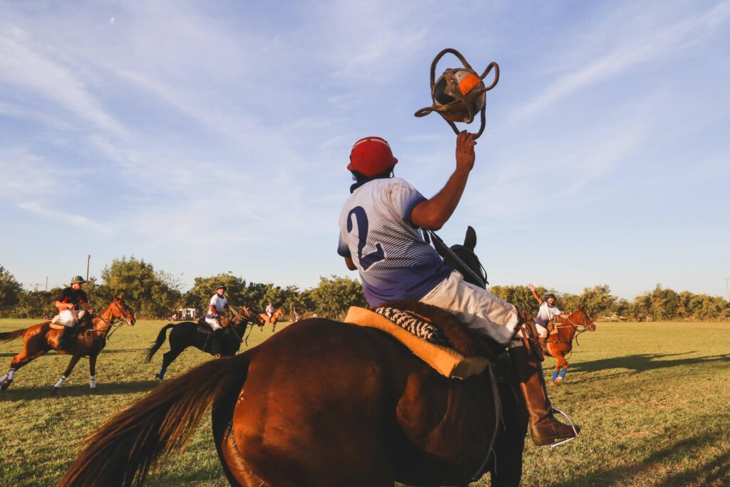 A man on horseback flings a ball back to throw it forward to thee men on horseback waiting