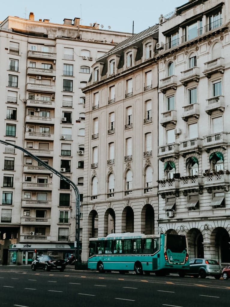 A teal bus drives down a road by French-style apartment buildings