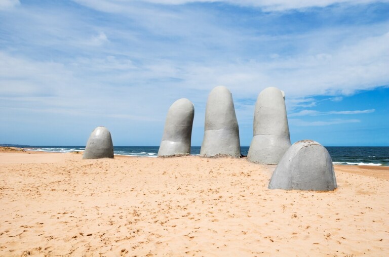 A statue of five fingers poking out of the sand on the beach