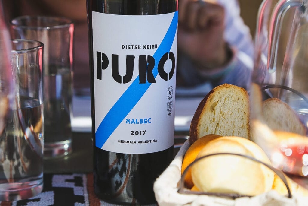 A bottle of wine on a table next to a basket of bread