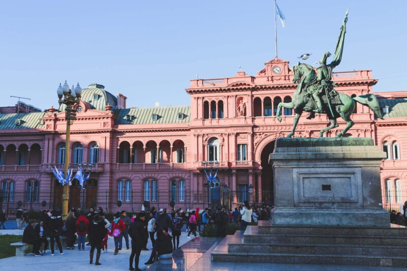 A statue of a man on a horse on a pedestal in front of La Casa Rosada government building