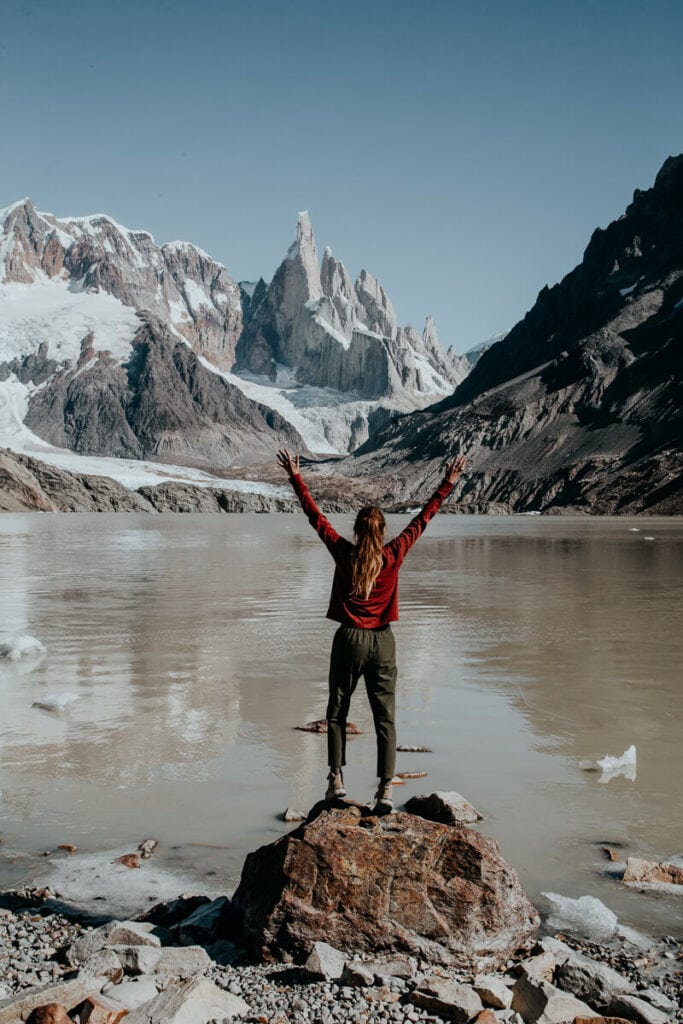 A woman stands on a rock in front of a lake in the mountains