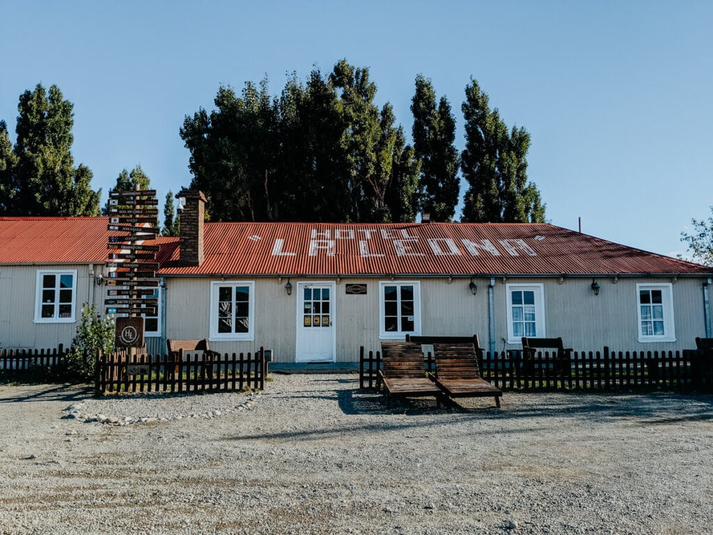 A yellow building with a red roof with pine trees behind it