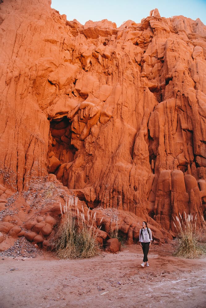 A woman standing in front of a red stone formation at the Cuevas de Acsibi in Argentina