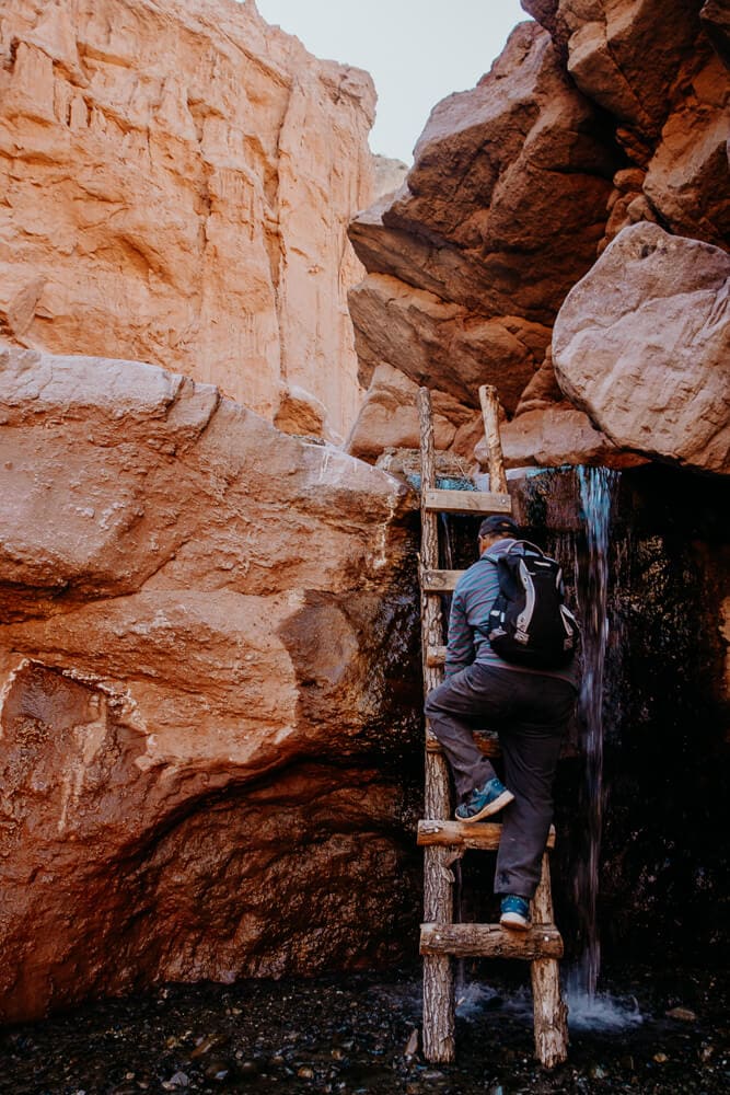 A man climbs a wooden ladder by a waterfall