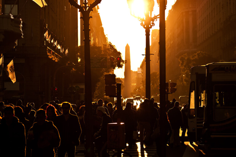 A sea of people walk down a road at sunset