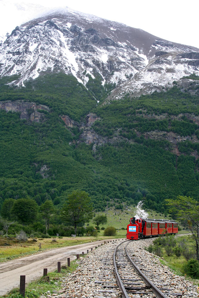 A red steamer train in front of a green mountain