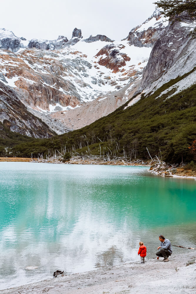 A man and his son crouch by a turquoise lagoon in the mountains