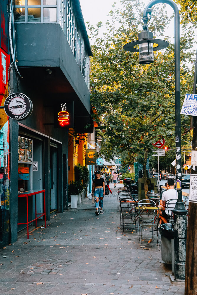 A woman walks down a sidewalk by stores in Palermo Soho Argentina