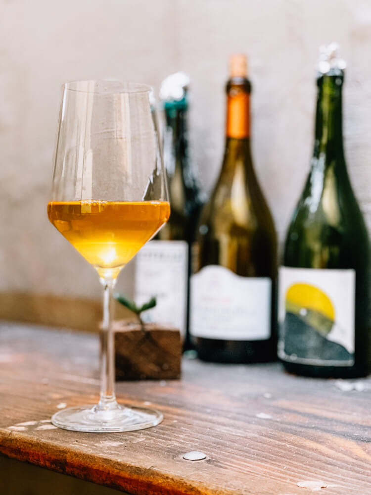 A glass of white wine on a wooden table in front of three bottles