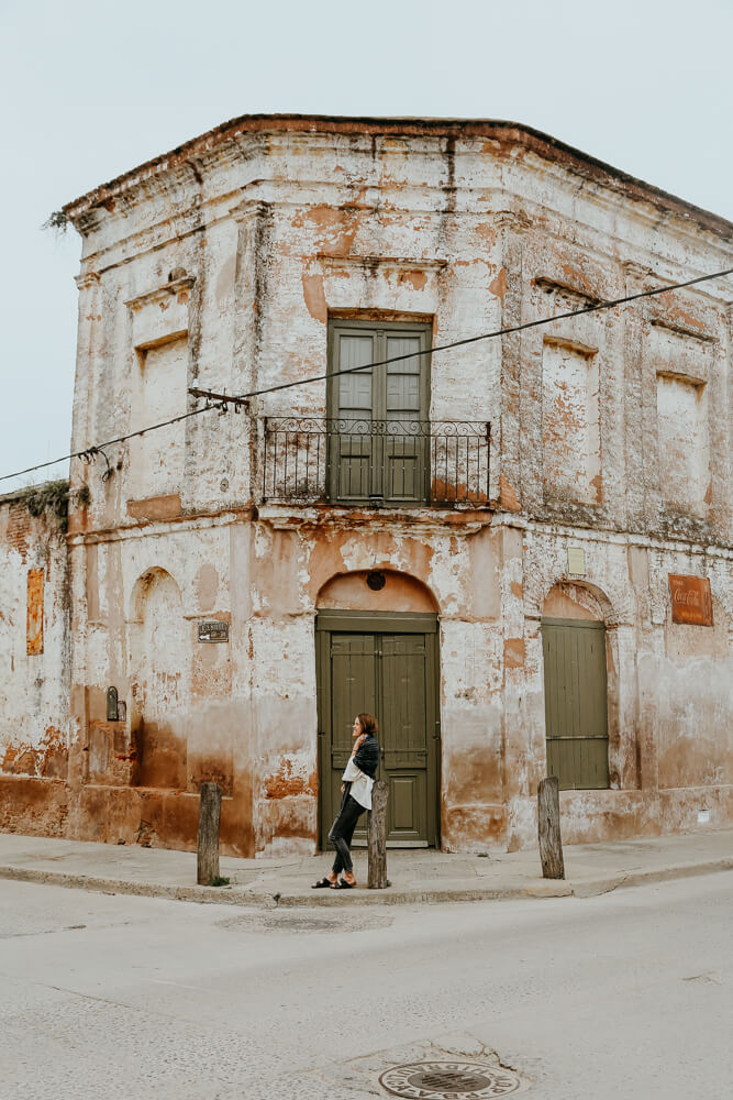 A woman leans against a post in front of an old building