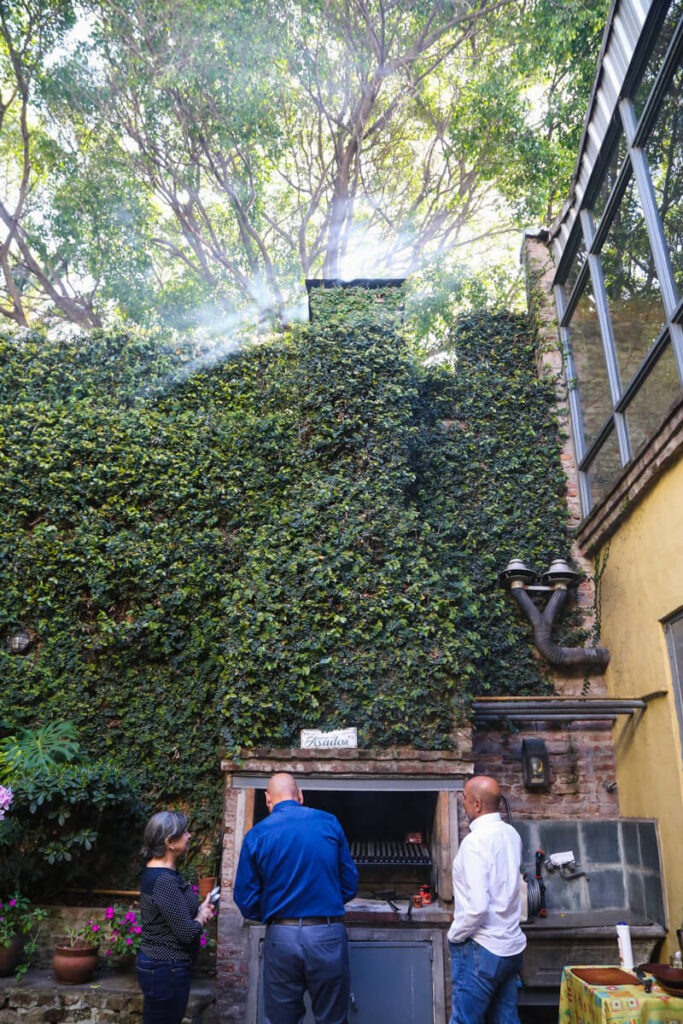 Two men and a woman stands around a parrilla in Buenos Aires at an asado