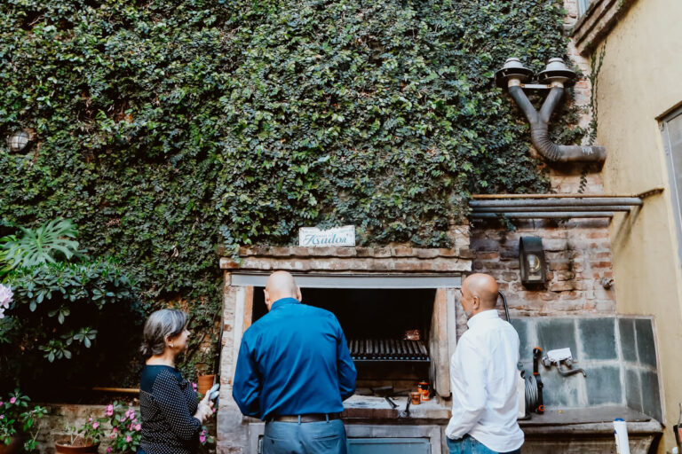 Two men and a woman around a parrilla at an Argentina asado in Buenos Aires