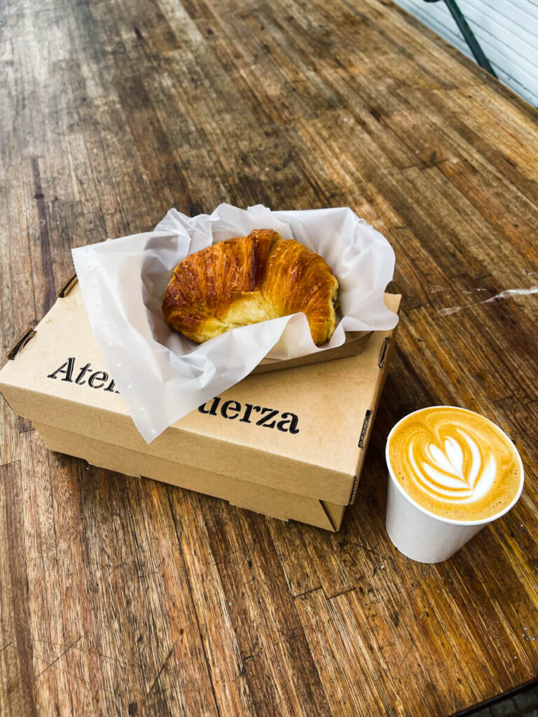 A medialuna pastry on a cardboard box on a wood table by a cup of coffee