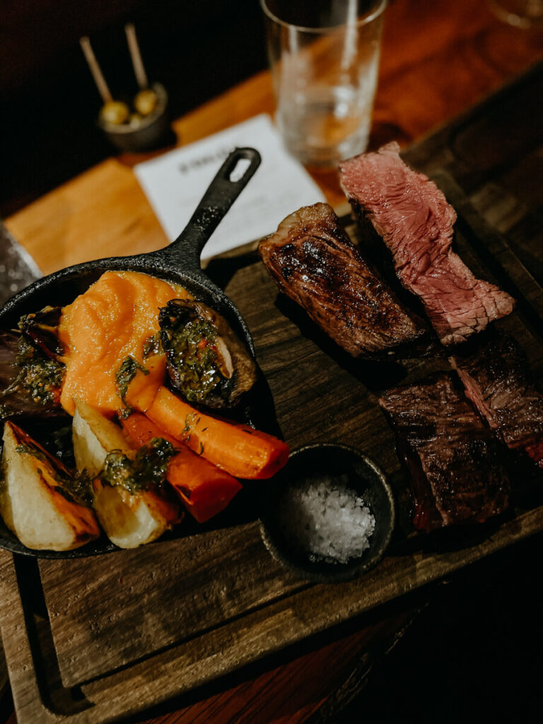 A wooden plate with steak and grilled vegetables