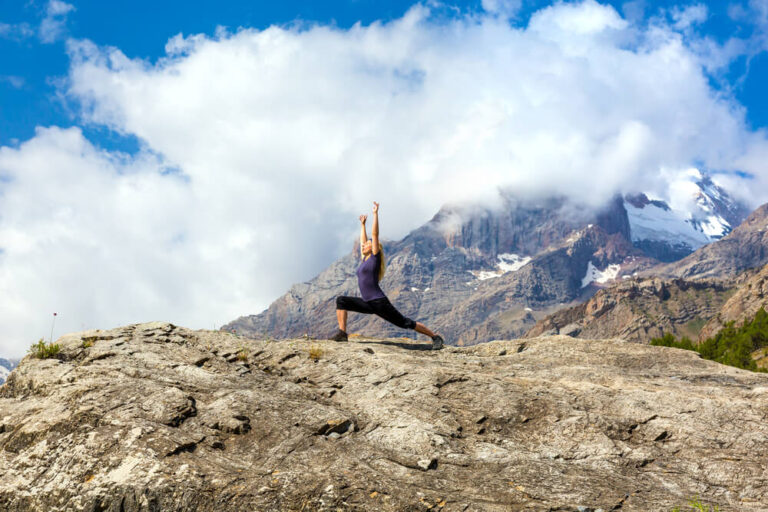 A woman in high lunge and arms stretched high atop a mountain