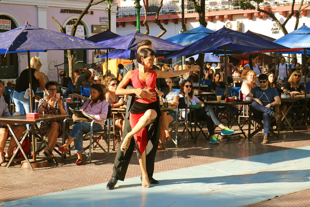 Two tango dancers perform in a public square in front of outdoor diners