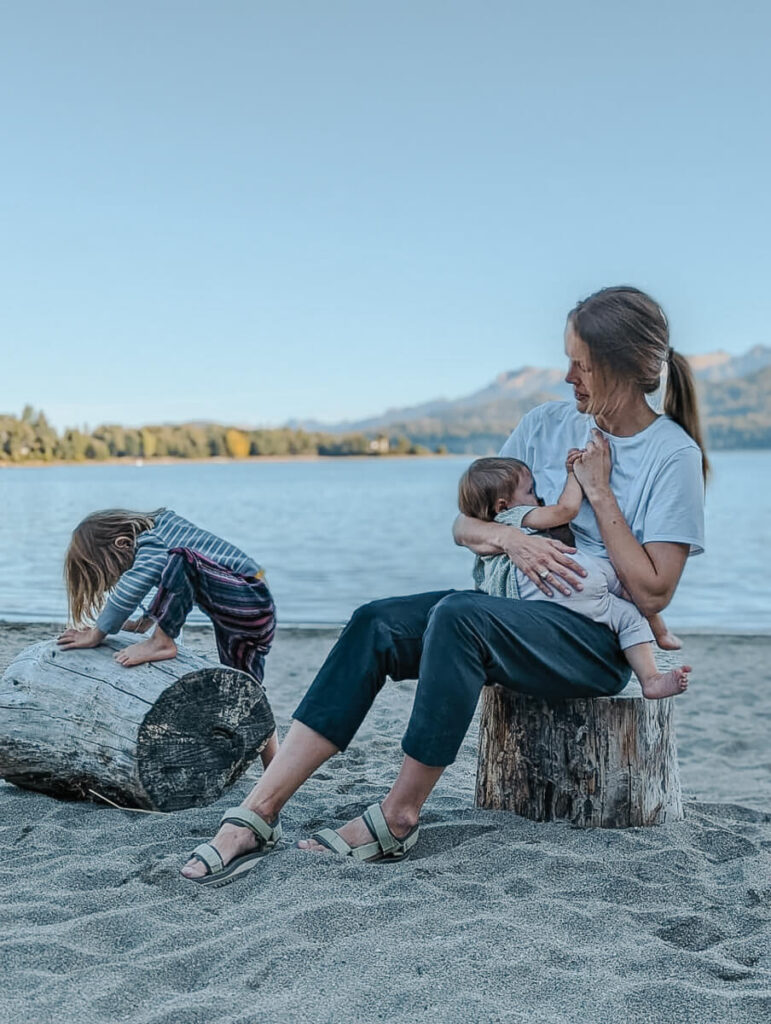 A woman sits nursing her baby while her older child plays next to them