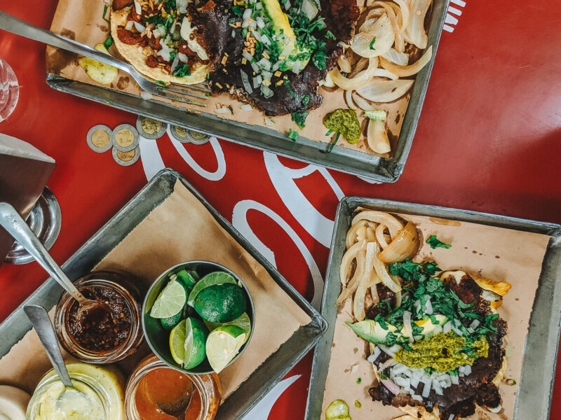 A red coca cola table with three platters filled with tacos and sauces
