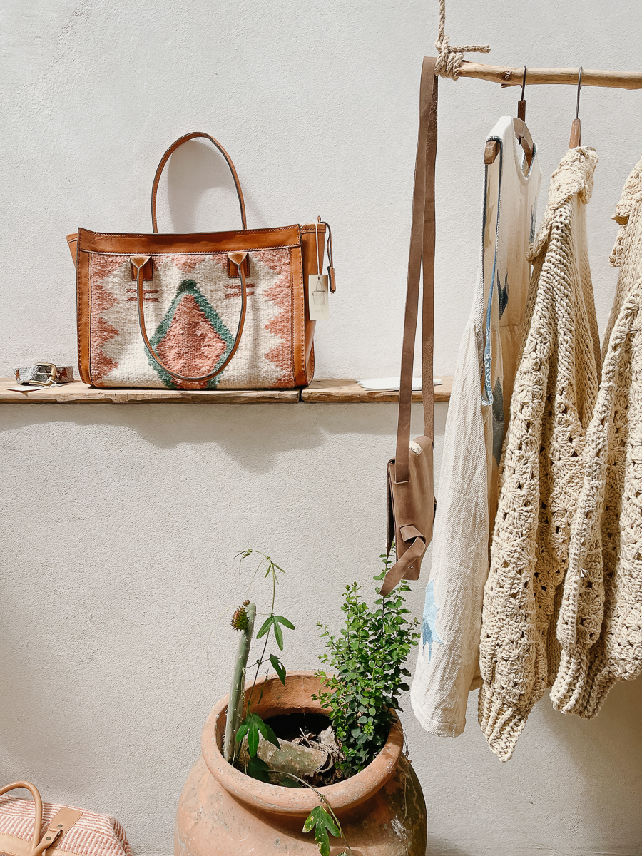 A leather bag and a shelf of dresses in a white room