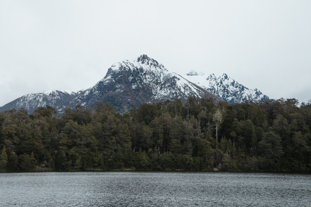 A snow covered mountain with a forest stand in the background of a lake